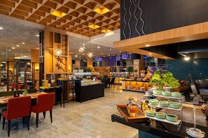 A modern restaurant with a high ceiling, wooden paneling, and a variety of seating options including tables and chairs. - BATIQA Hotel & Apartments Karawang (Karawang)