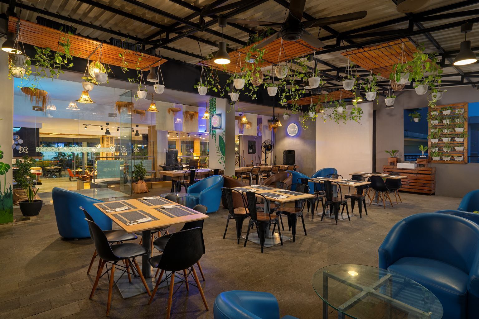 A restaurant with tables and chairs, hanging plants, and a ceiling fan.