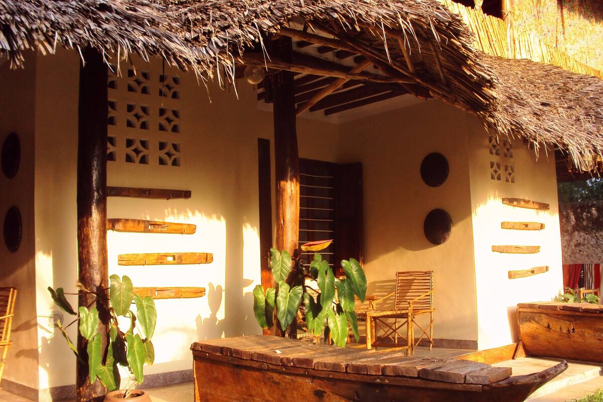 Un área de estar al aire libre rústica con techo de paja, muebles de madera y plantas en macetas.