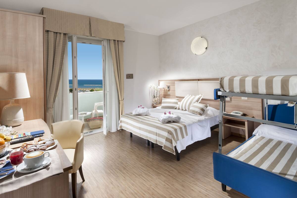 Ein Hotelzimmer mit Bett, Schreibtisch mit Frühstück, einem Sessel und Meerblick.