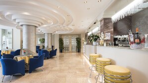 Eine moderne Hotelhalle mit Marmorböden, blau-gelben Sitzgelegenheiten, einer Bar und dekorativen Pflanzen.
