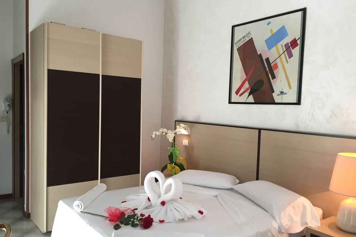 Ein Hotelzimmer mit einem Bett, einem Kleiderschrank, einem Wandbild und einem Nachttisch mit Lampe.