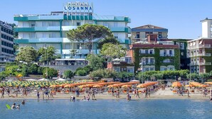 Ein mehrstöckiges Hotel namens 'Hotel Losanna' mit Außenbereich und einem Strand im Vordergrund.