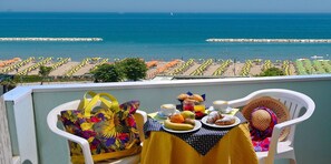 Een balkon met een ontbijtset, uitkijkend op een strand met parasols en een rotsenrij.