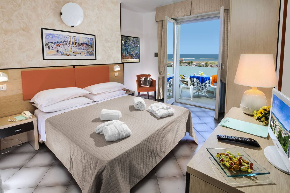 Ein Hotelzimmer mit Bett, Schreibtisch mit Lampe, Stuhl und Meerblick.
