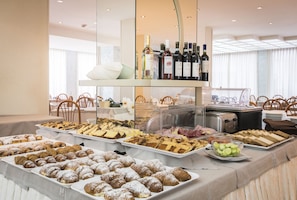 Een buffet met diverse gebakjes en desserts, een selectie wijnflessen en een zithoek met stoelen.
