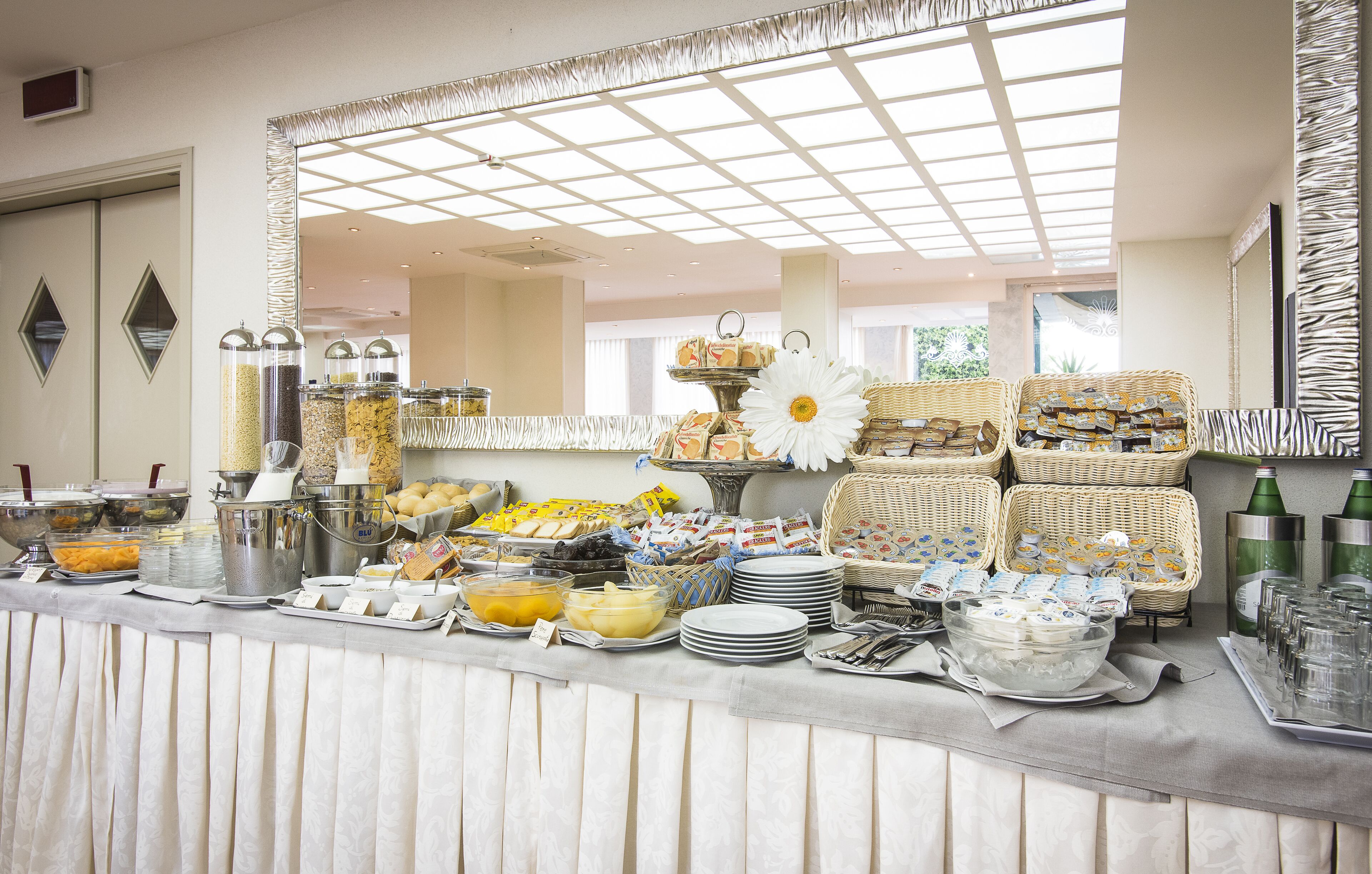 A buffet setup with various food items and beverages, including bowls of cereal, fruits, and sandwiches.
