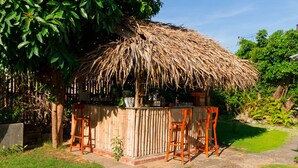 A thatched-roof outdoor bar area with wooden stools and a bamboo fence.