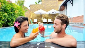 A couple in a swimming pool with umbrellas and lounge chairs in the background.