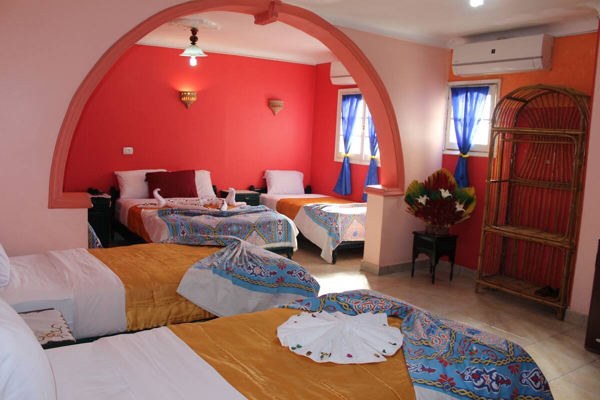A hotel room with two beds, a sitting area, and a decorative plant.