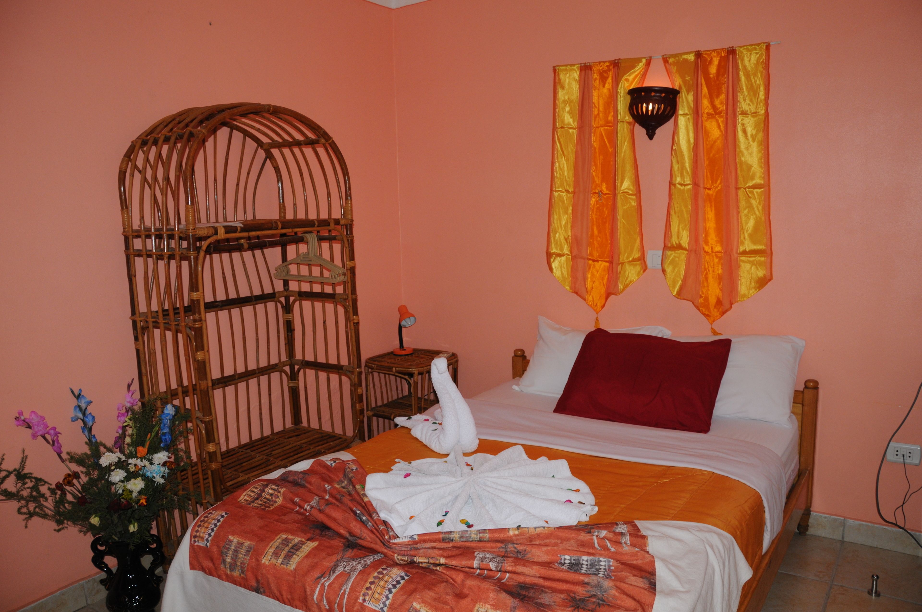 Una habitación con cama, una silla de madera, una mesita, una lámpara de pared y una cortina.