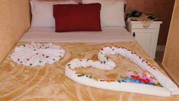 A hotel room with a neatly made bed, a red pillow, and a white bedside table with a phone and a decorative item.