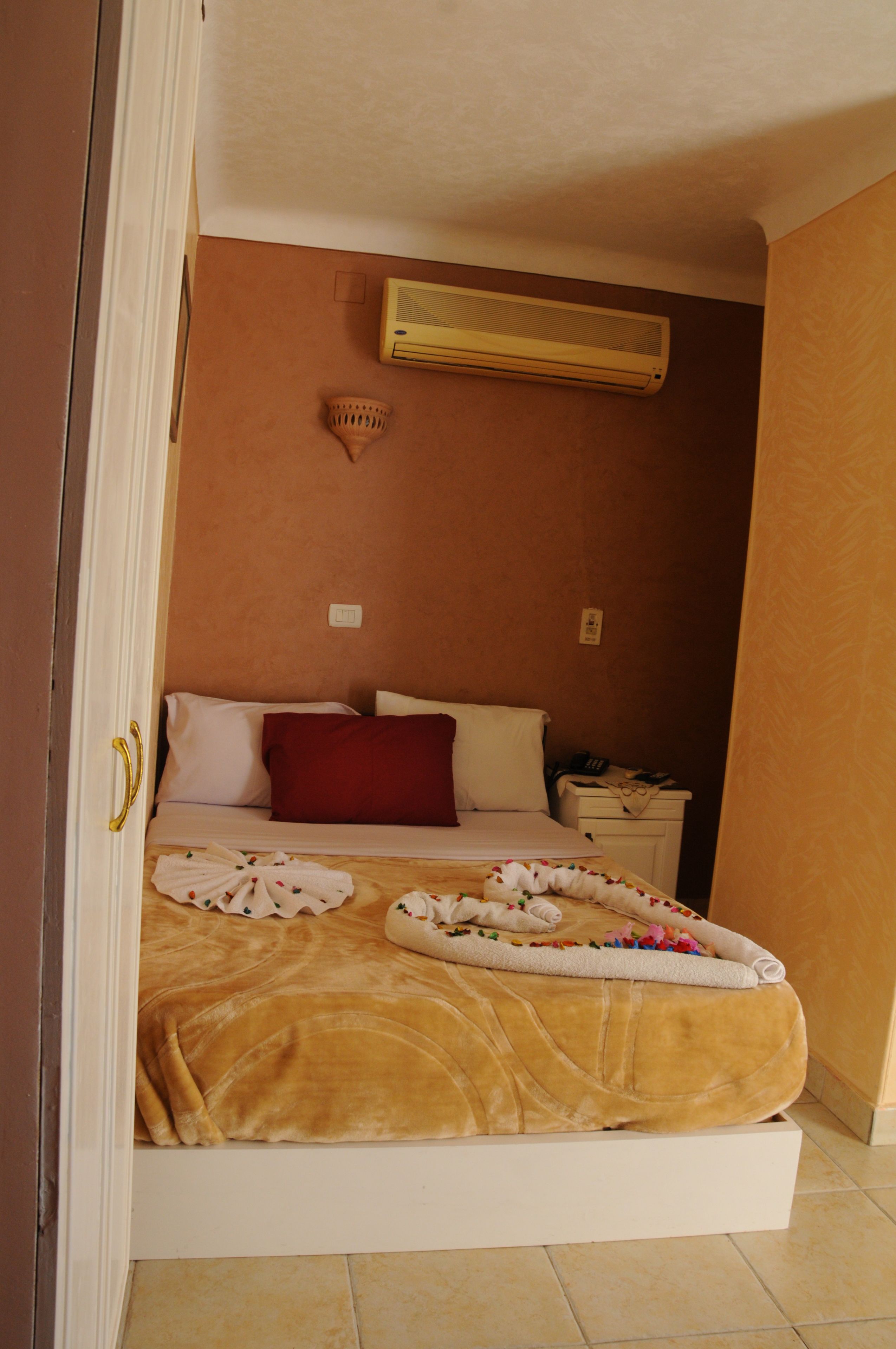 Un dormitorio con cama, almohadas, mesita de noche y aire acondicionado.