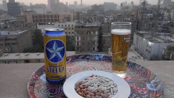 A can of Stella beer, a glass of beer, and a plate with nuts on a table with a cityscape view.