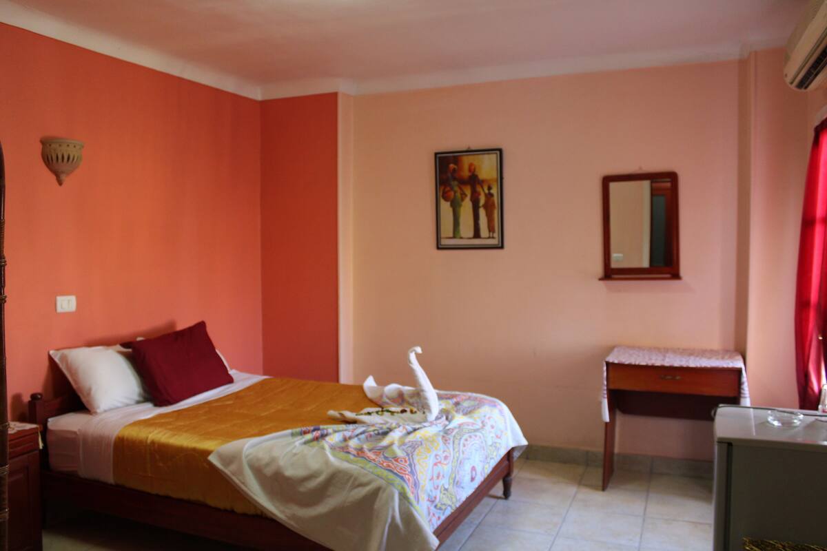 A hotel room with a bed, a small desk, a mirror, and a wall-mounted picture.