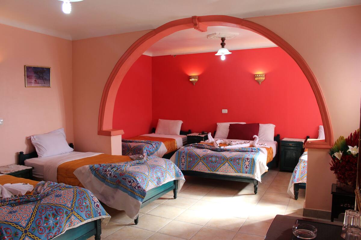 A hotel room with two beds, a red accent wall, and a decorative arch.