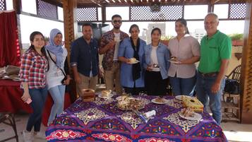 A group of people standing around a table with various desserts under a wooden pergola.