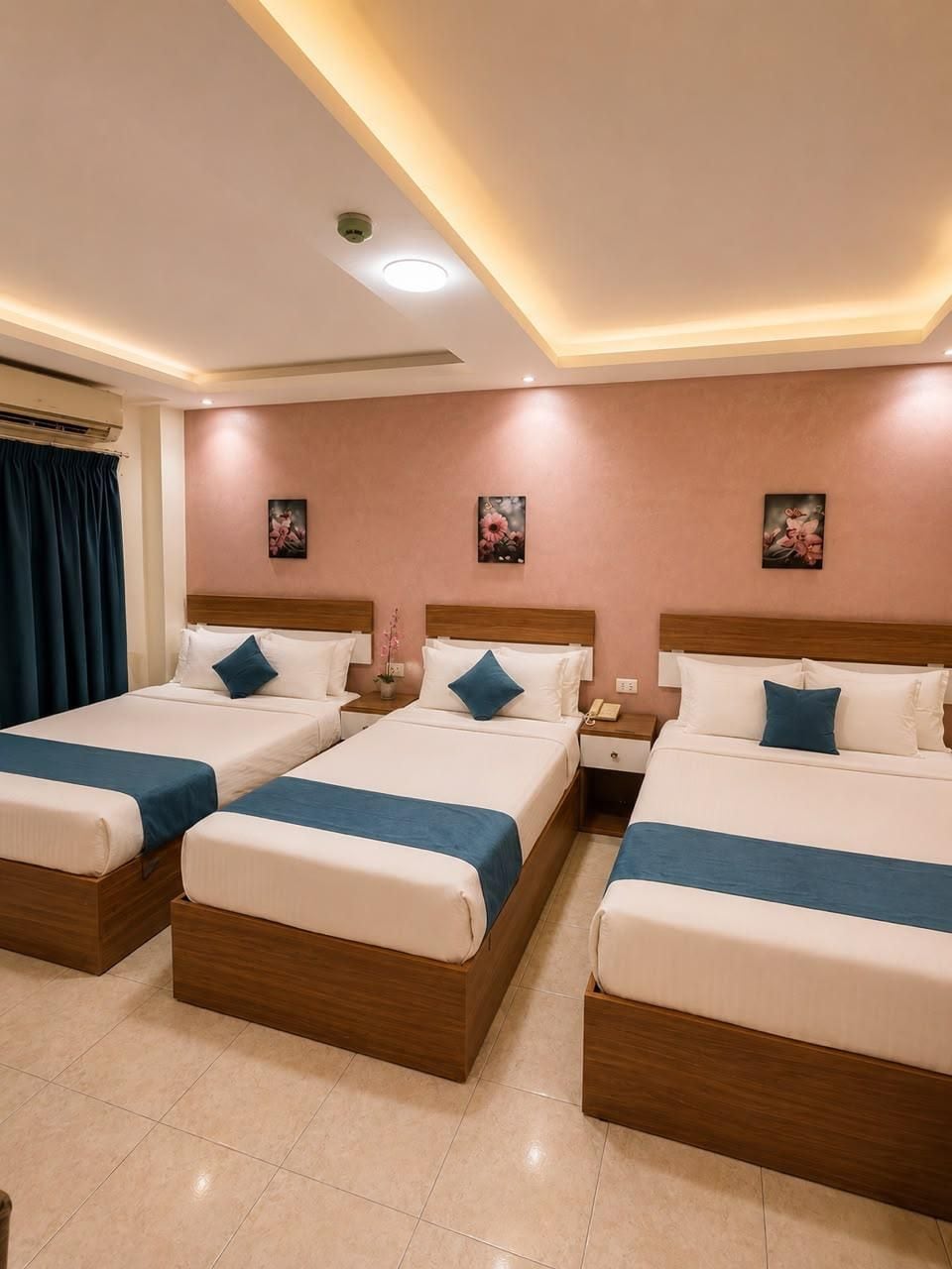 A hotel room with three beds, each with a wooden headboard, white bedding, and blue accents.