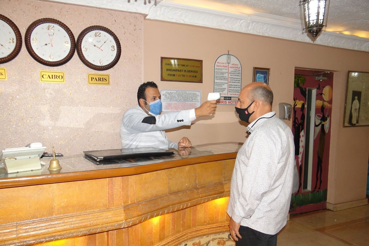 A hotel reception area with clocks labeled 'CAIRO' and 'PARIS,' a check-in counter, and a sign indicating breakfast service times.