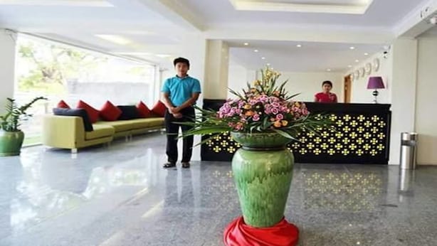 A hotel lobby with a reception desk, a sofa with red cushions, and a large green vase with flowers. - The Hotel 78 (Mandalay)