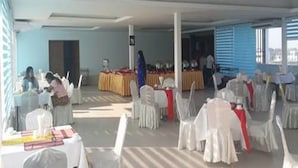A spacious hall with white chairs arranged in rows, a long table with a yellow tablecloth, and a person standing near the table. - The Hotel 78 (Mandalay)