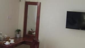 A bathroom with a wooden vanity, a mirror, a flat-screen TV mounted on the wall, and a small potted plant. - The Hotel 78 (Mandalay)