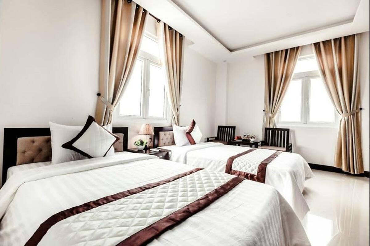 Ein Hotelzimmer mit zwei Betten, beigen Vorhängen, einem Nachttisch, einer Lampe und einem Fenster.