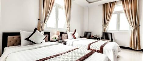 A hotel room with two beds, beige curtains, a nightstand, a lamp, and a window.