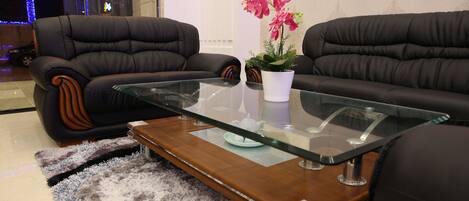 A modern living room with two black leather sofas, a glass coffee table, and a potted orchid.