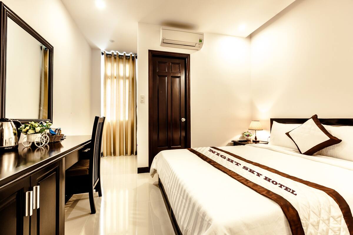 Ein Hotelzimmer mit Bett, Schreibtisch, Stuhl, Spiegel, Tür und Klimaanlage.