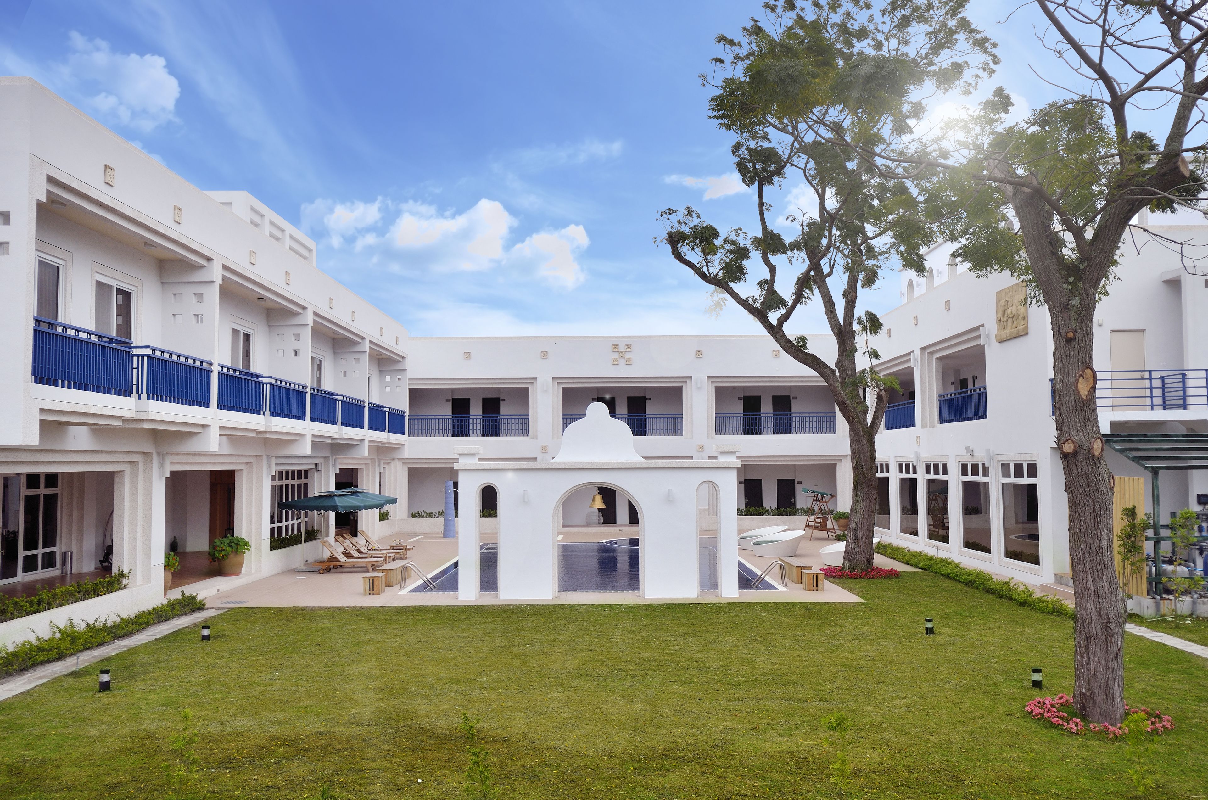 A courtyard with a pool, white buildings, and a tree.