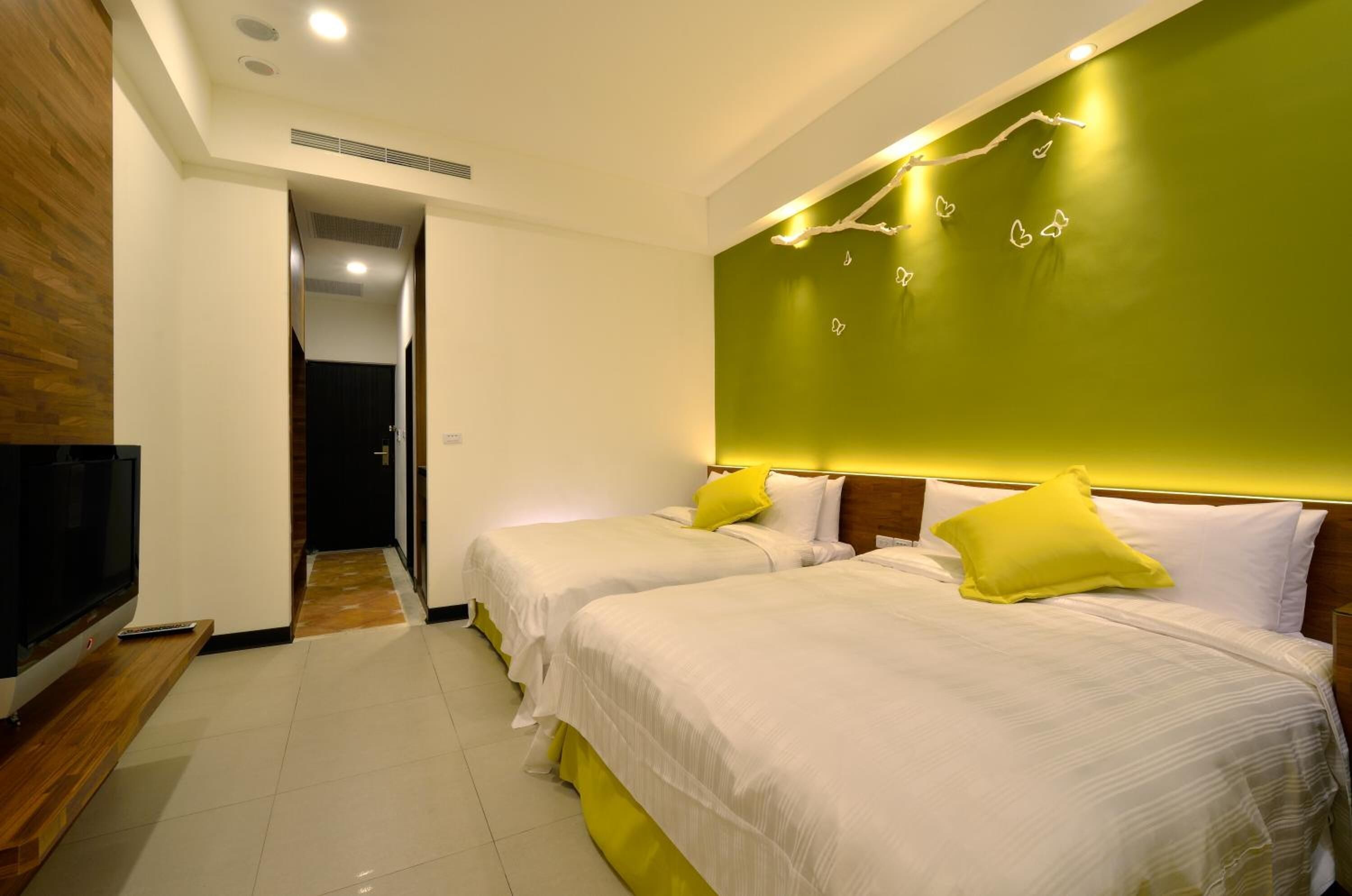 Habitación de hotel con dos camas, un televisor y una pared de acento verde.