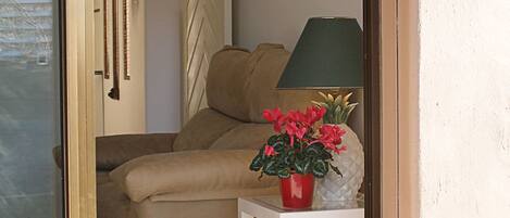 Et værelse med en sofa, et lille hvidt bord med en rød blomsterpotte, en grøn lampe og en vægmonteret lysarmatur.
