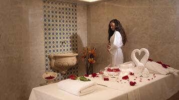 A spa room with a massage table, a decorative wall, and a vase of flowers.