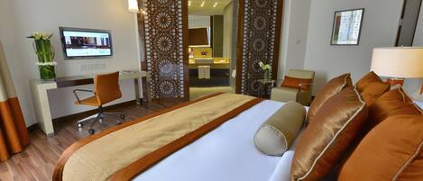 A hotel room with a large bed, a desk with a computer, a chair, and a bathroom visible through a doorway.
