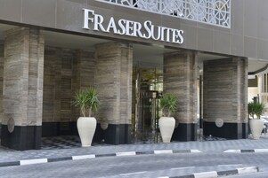 Exterior de un hotel llamado "FrasersSuites" con diseño moderno, que cuenta con columnas grandes y plantas en macetas.