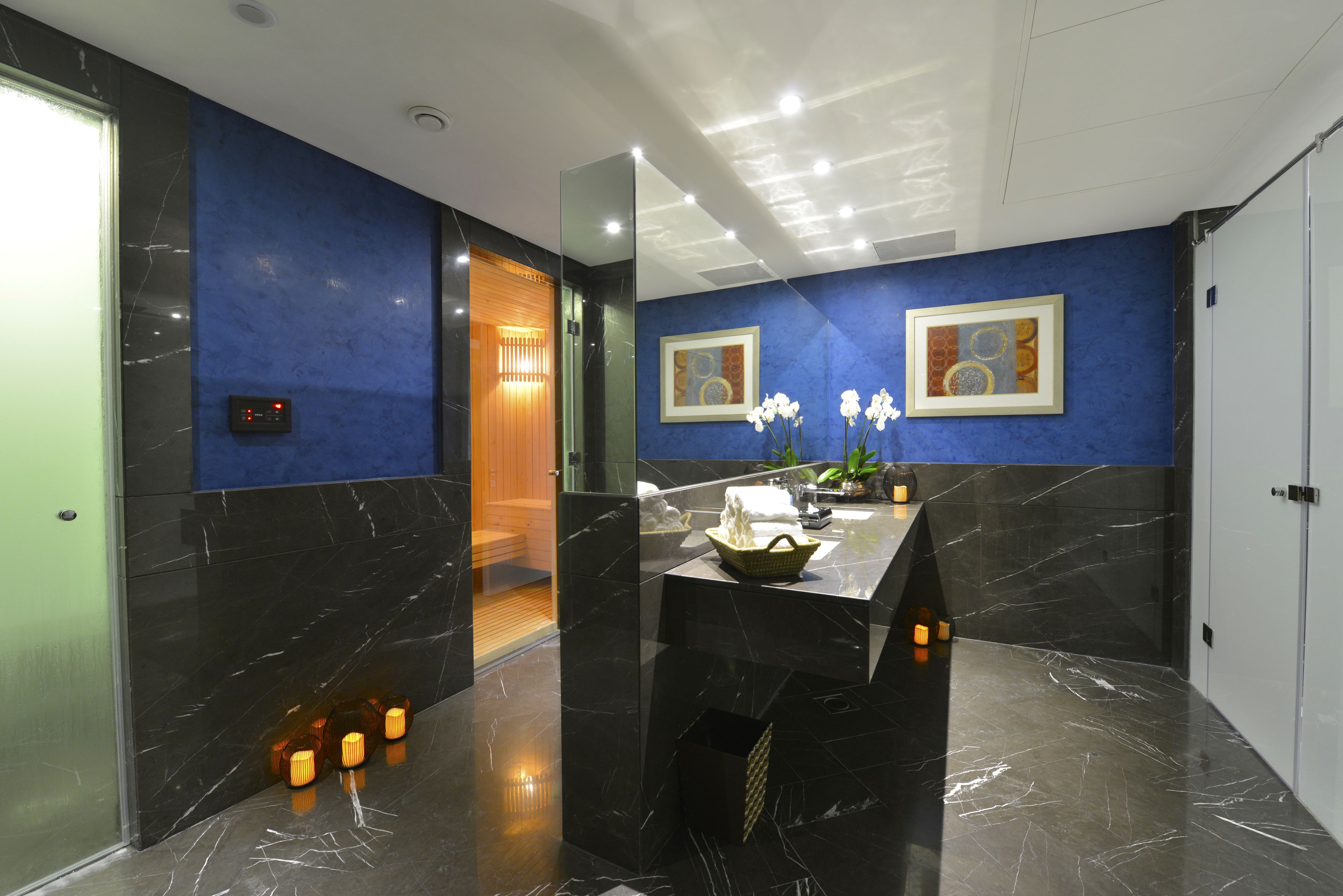 A modern lobby with marble floors, a reception desk, framed artwork, and a wooden door leading to a sauna area.