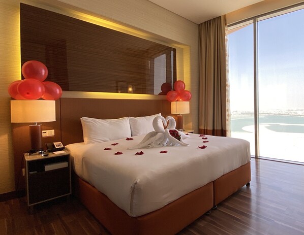 A hotel room with a large bed, two bedside lamps, a nightstand, and a view of a body of water.