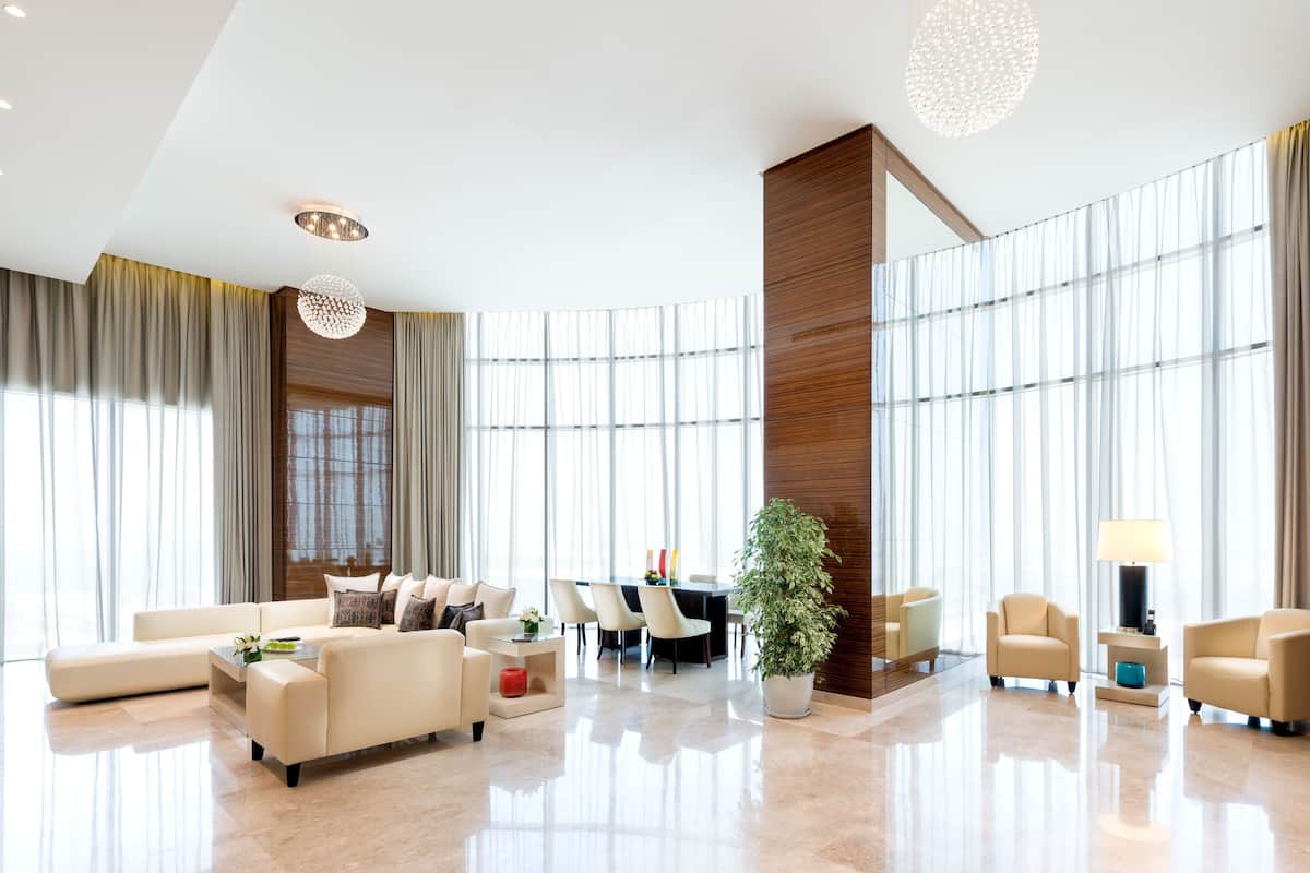 A spacious lobby with a high ceiling, large windows, a central seating area, and a modern chandelier.
