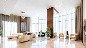 Un vestíbulo amplio con techo alto, ventanas grandes, una zona de estar central y un candelabro moderno.