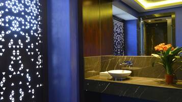 Un baño moderno con lavamanos de mármol, una planta en maceta y una pared decorativa con patrones geométricos.