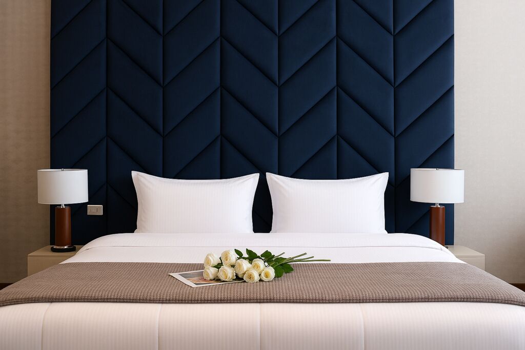 A hotel room with a large bed, two bedside lamps, a dark headboard, and a bouquet of white flowers on the bed.