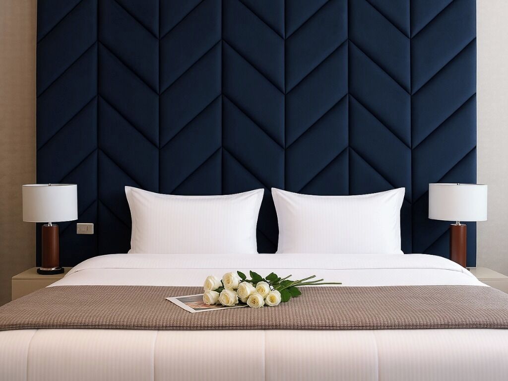 A hotel room with a large bed, two bedside lamps, a dark blue headboard, and a bouquet of white flowers on the bed.