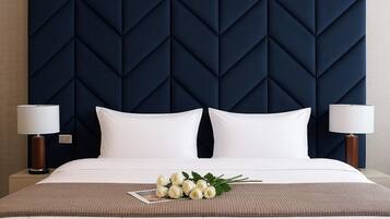A hotel room with a large bed, two bedside lamps, a dark blue headboard, and a bouquet of white flowers on the bed.