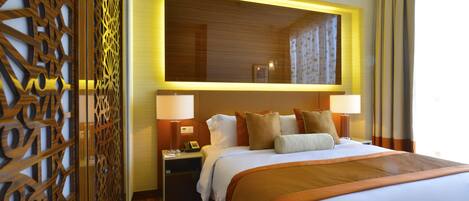 Habitación de hotel con una cama grande, dos mesitas de noche, una separador de madera y un espejo grande sobre la cama.