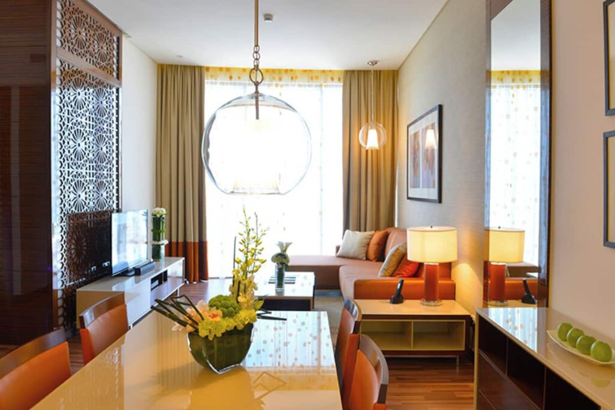 A hotel room with a dining table, chairs, a sofa, a TV, and a decorative wall panel.