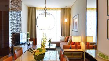 Una habitación de hotel con una mesa de comedor, sillas, un sofá, un televisor y un panel decorativo en la pared.
