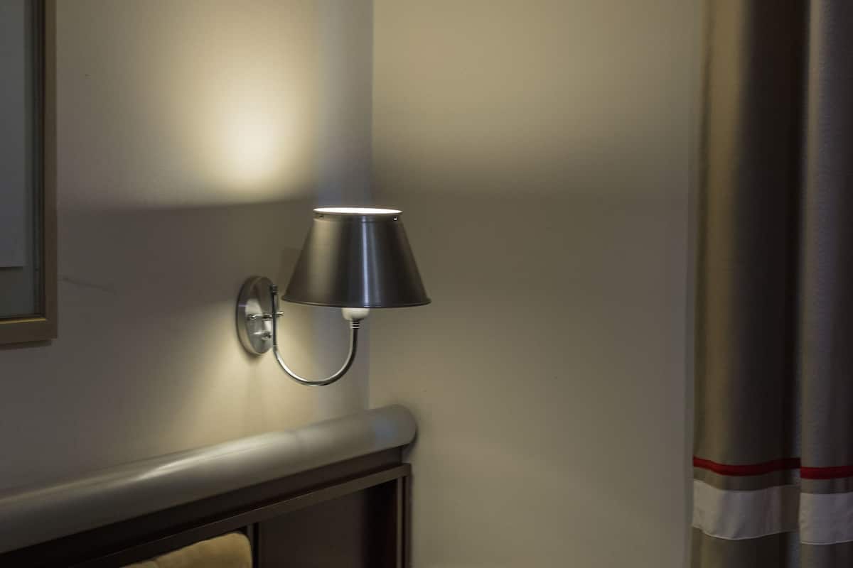 A hotel room with a bed, a nightstand, a lamp, and a curtain.