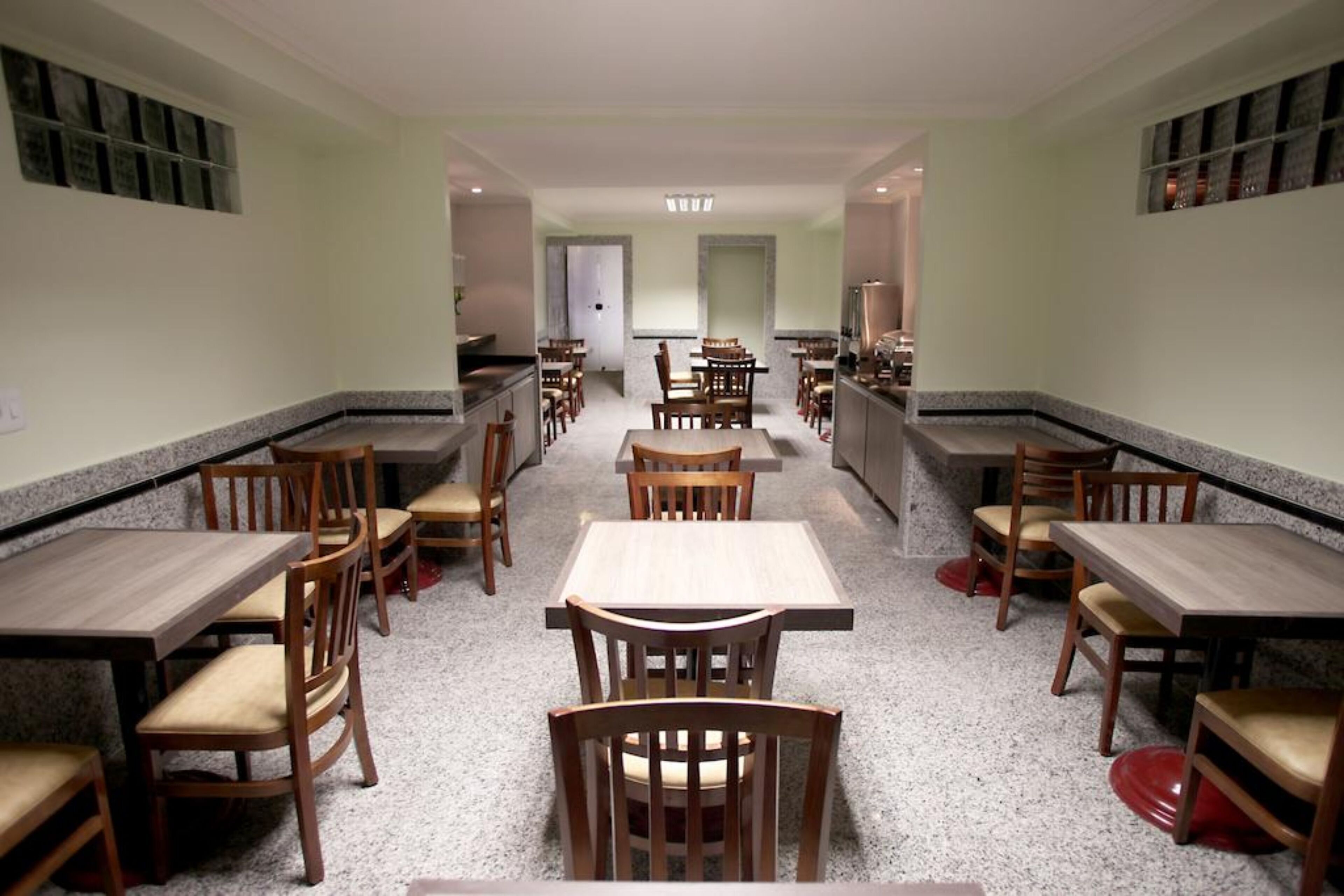 A spacious dining area with multiple tables and chairs, a central walkway, and a kitchen area in the background.