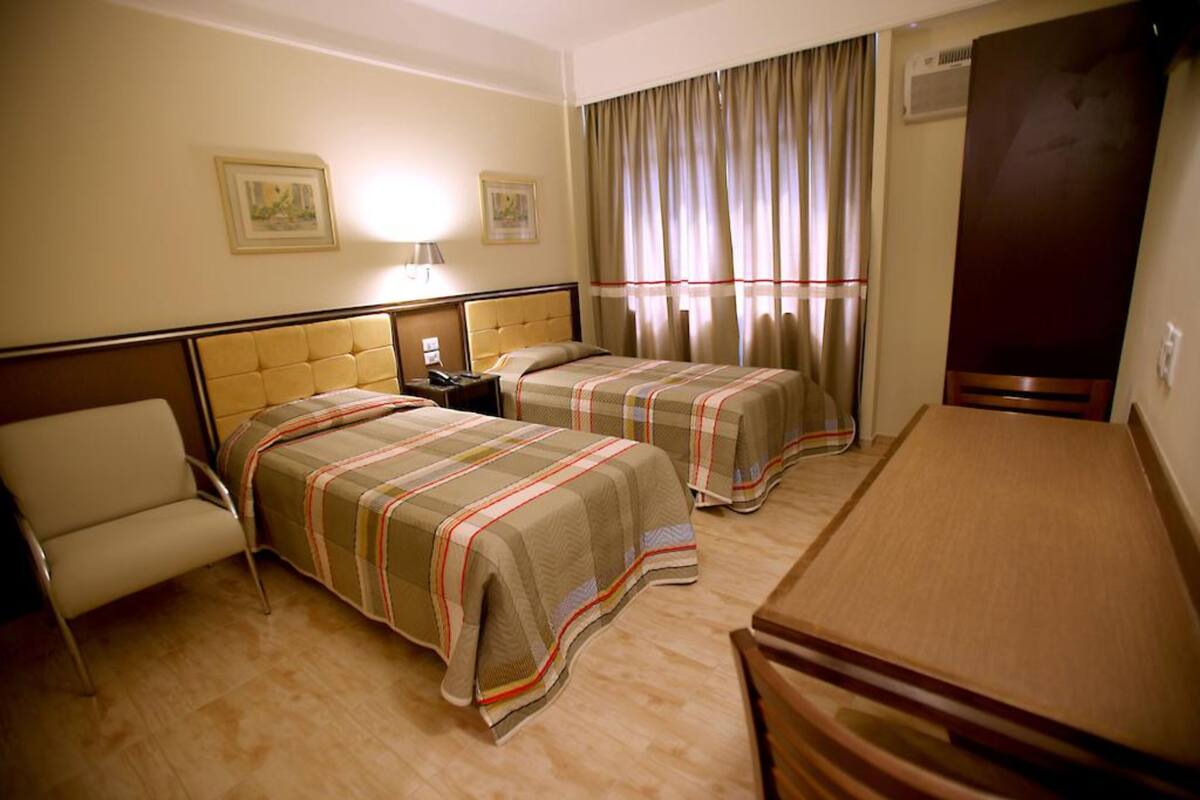 A hotel room with two beds, a desk, a chair, and a wardrobe.